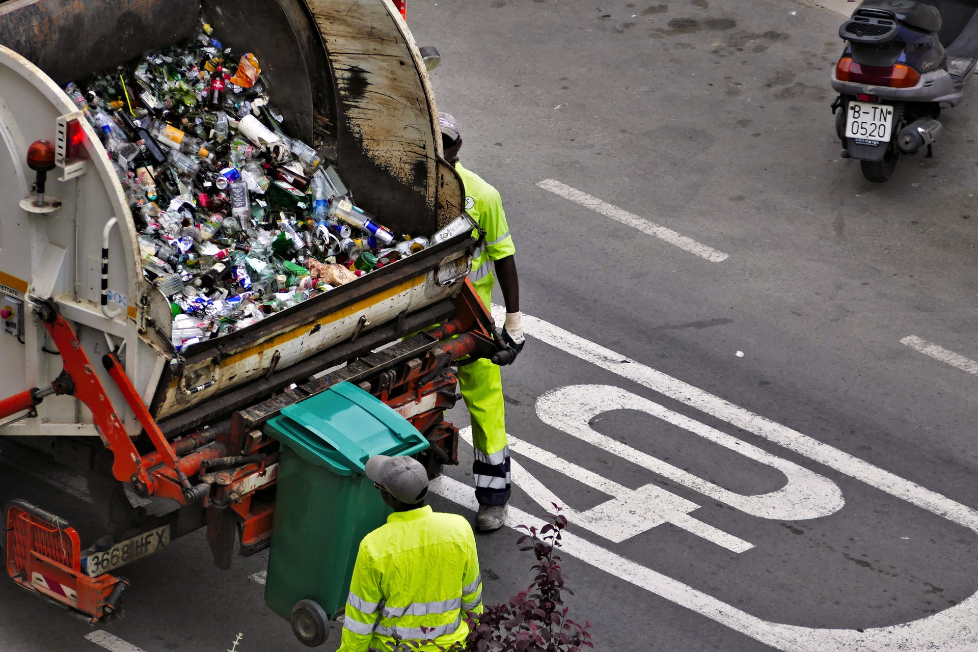 Los trabajadores usan equipo de protección personal mientras recogen basura con un camión de basura.